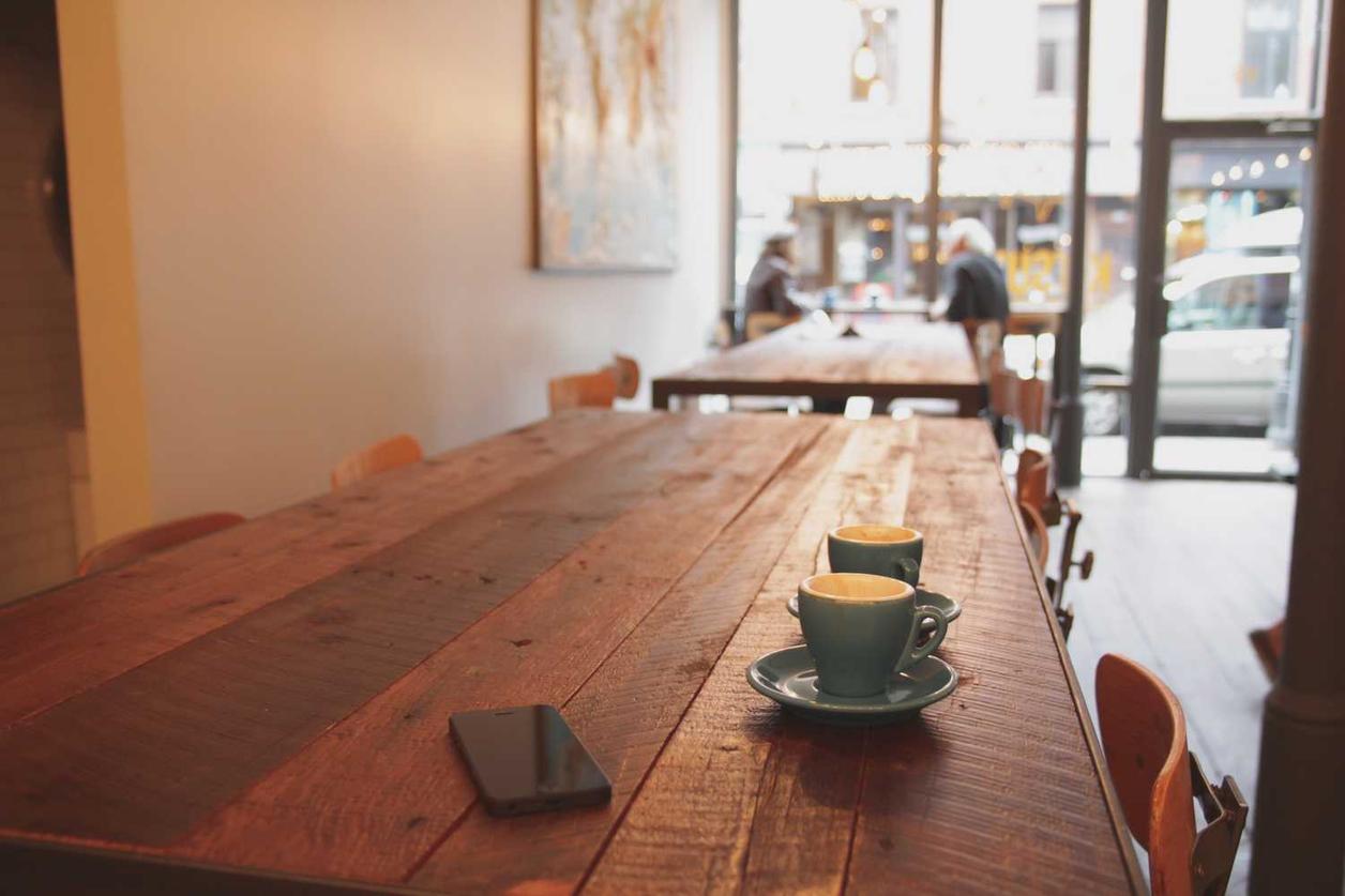 A rustic, long wooden table in a chill café with two turquoise cups a…