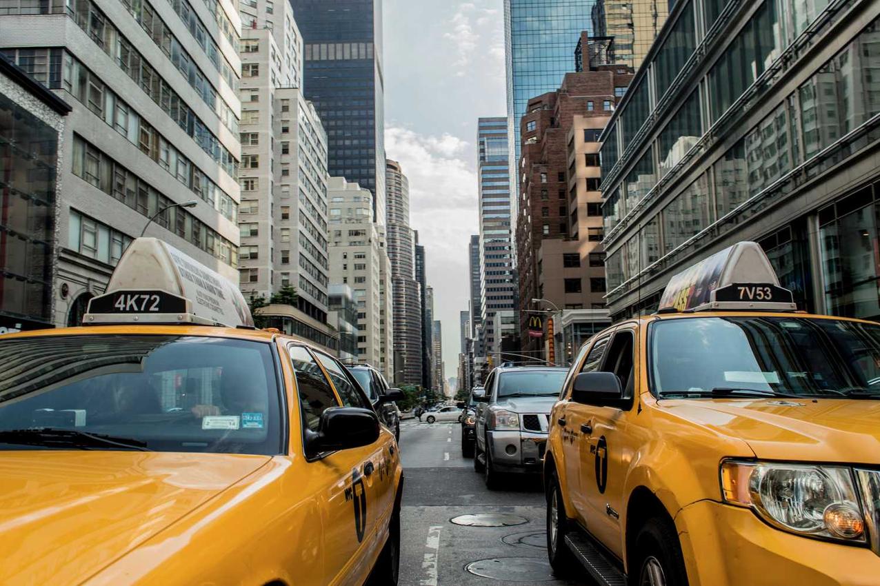 A bustling city street in the middle of the day with a yellow taxi cab…