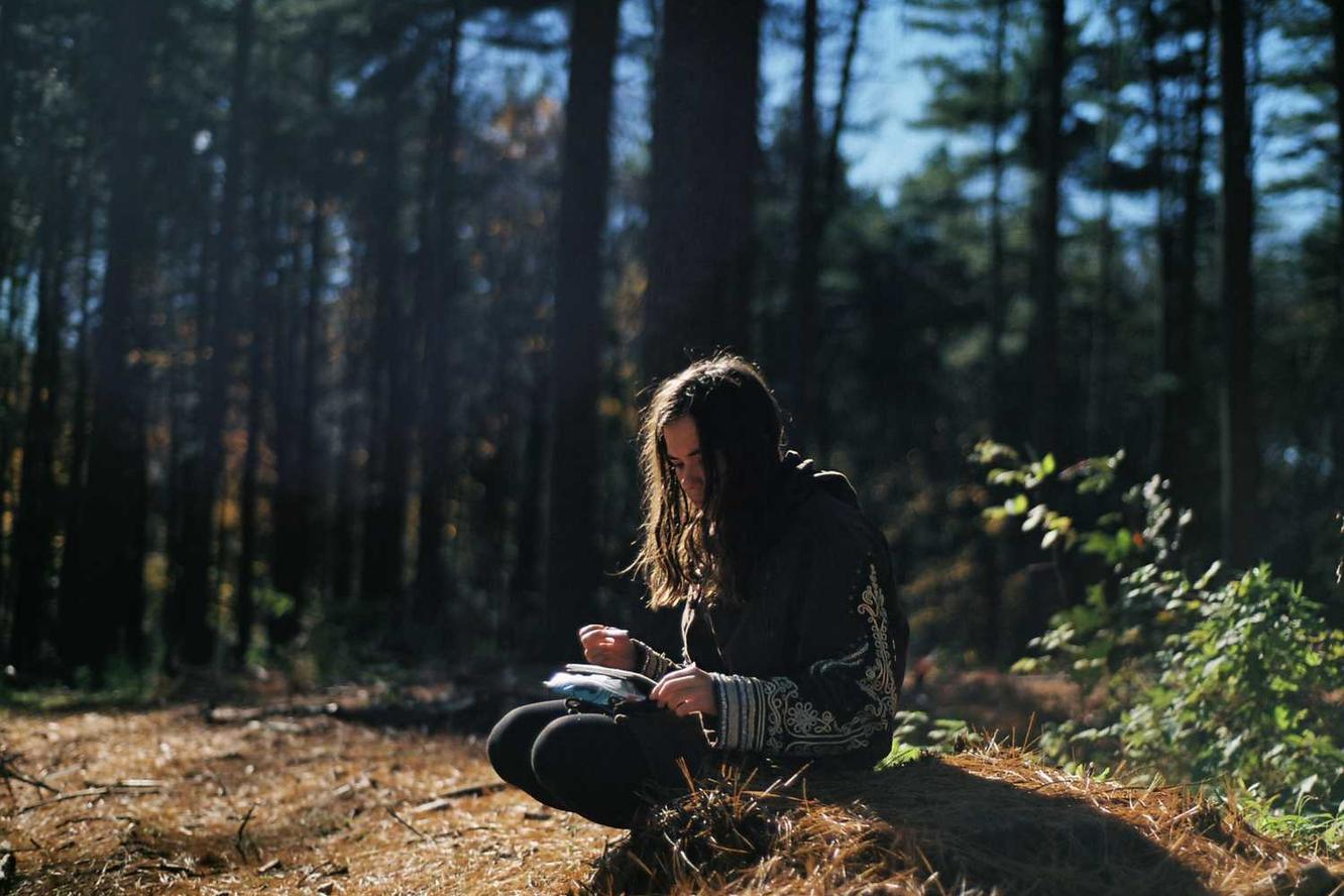 A young woman with long, wavy brown hair sits cross-legged on the fore…